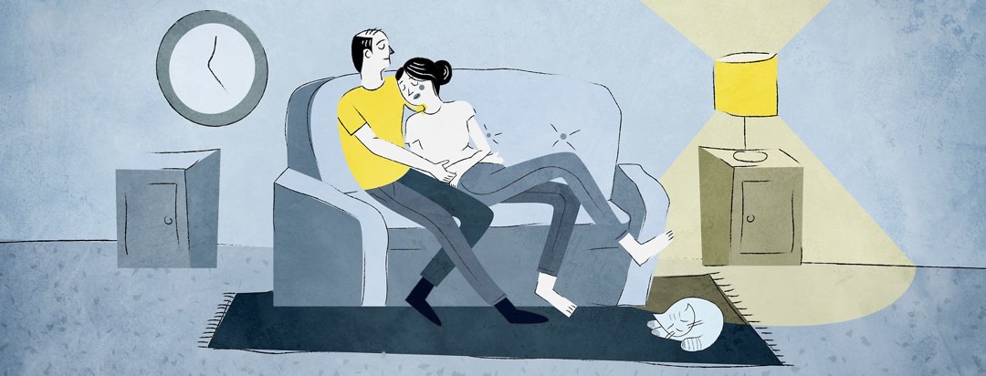 Couple sitting on their couch with one person comforting the other